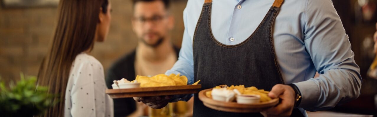 portrait-waiter-holding-plates-with-food-looking-camera-while-working-pub