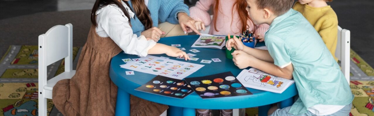 full-shot-kids-teacher-sitting-table.jpg